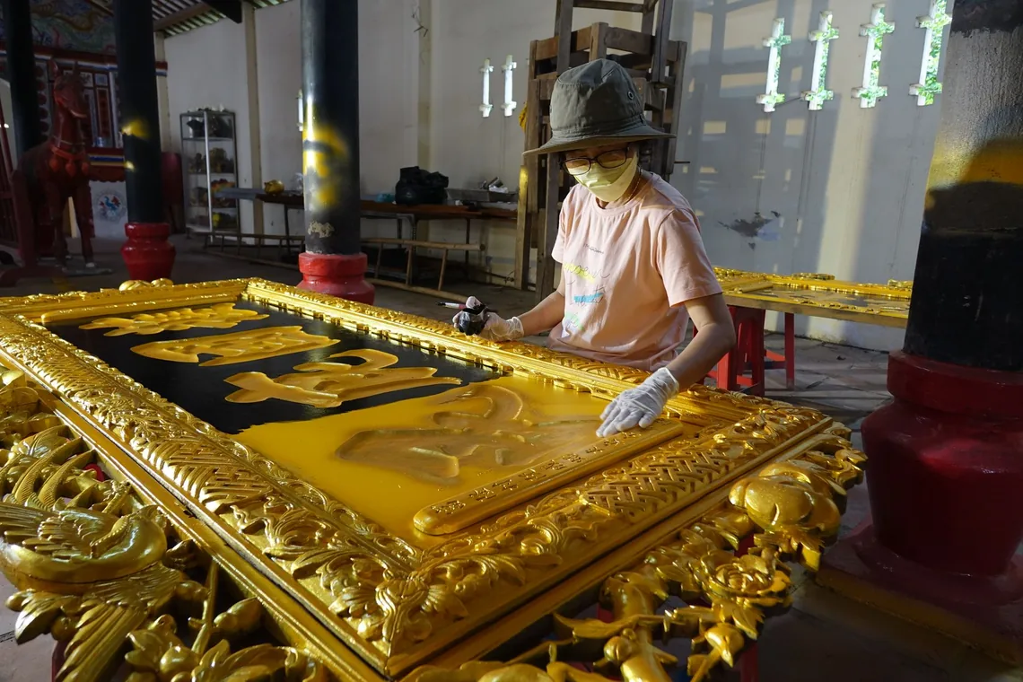 Artesano aplicando pan de oro sobre un panel decorativo tallado y dorado